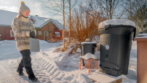 Nainen viemässä biojätettä kompostoriin aurinkoisessa talvisäässä.